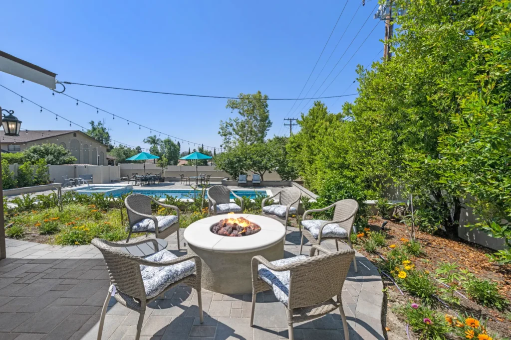 Backyard fire pit with lounge chairs, string lights and a pool beyond
