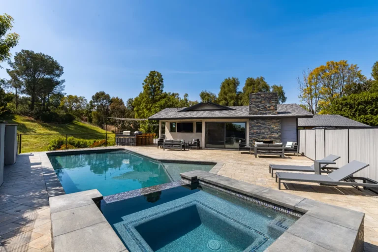 Single-story home exterior with a swimming pool, stone deck and covered patio